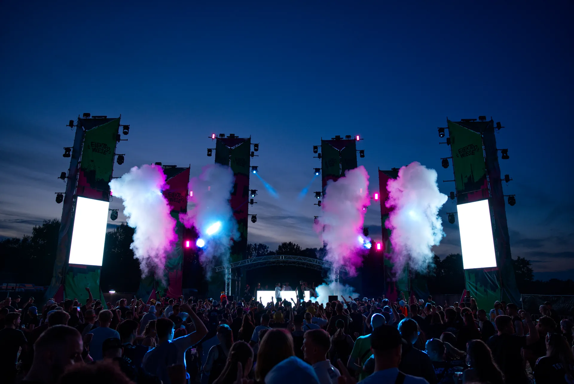 Festival crowd facing a stage filled with blue light and magenta smoke